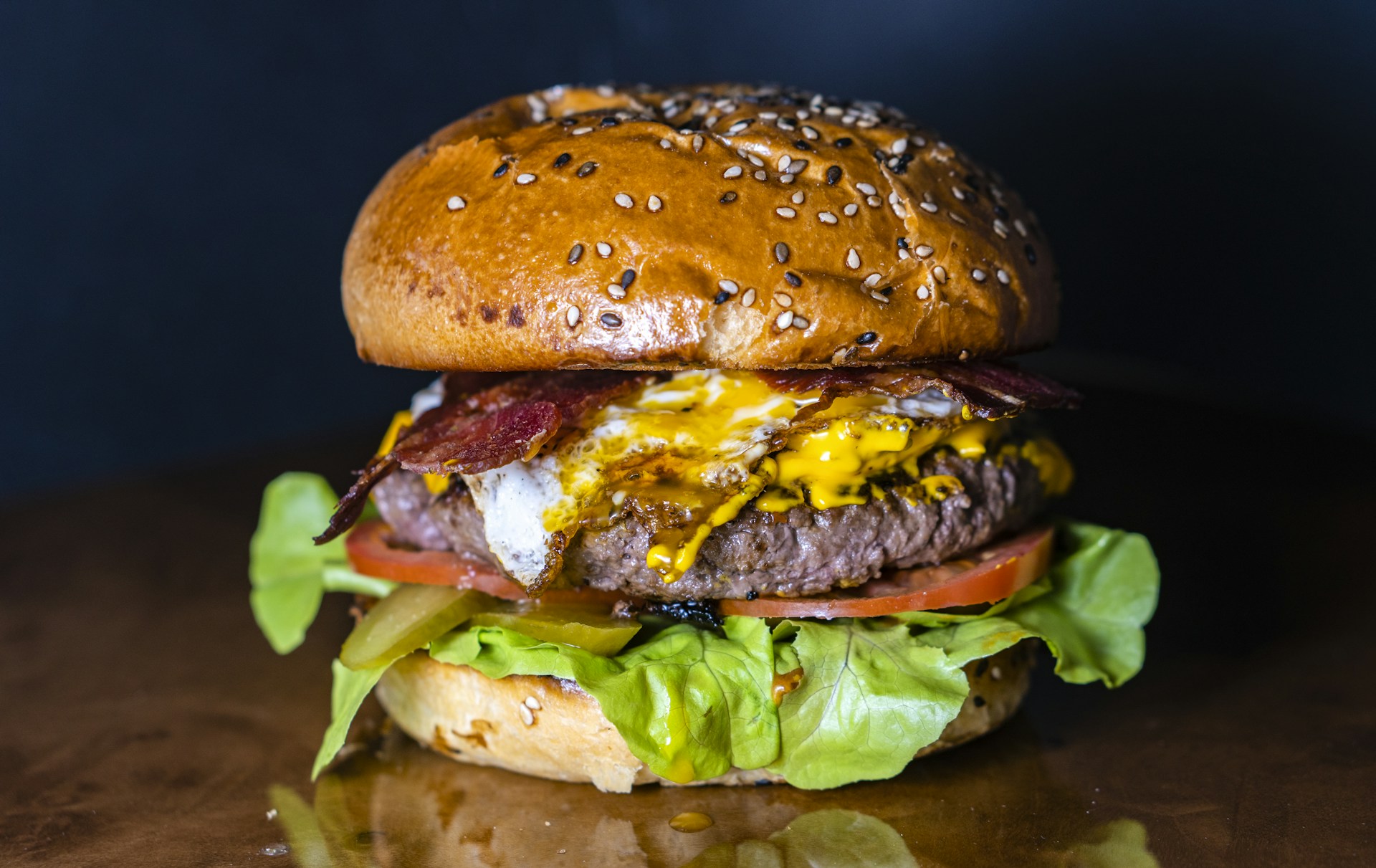 Frische Burger-Zutaten auf einem rustikalen Holzbrett — Brioche-Buns, Patty, Käse, Salat, Tomate und Zwiebel.